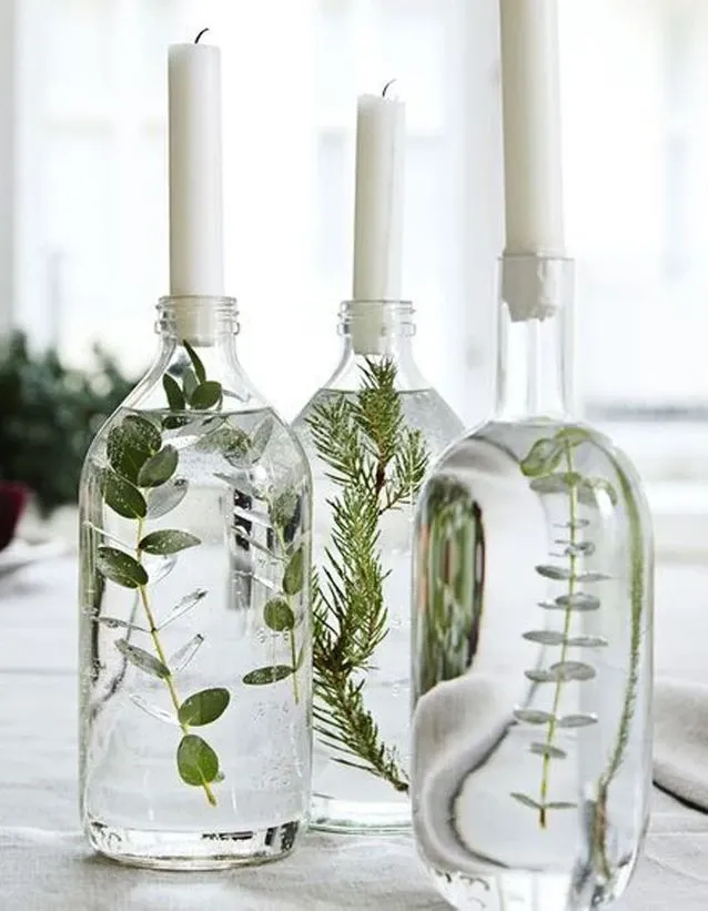 un groupe de bocaux en verre avec des feuilles vertes et des bougies blanches