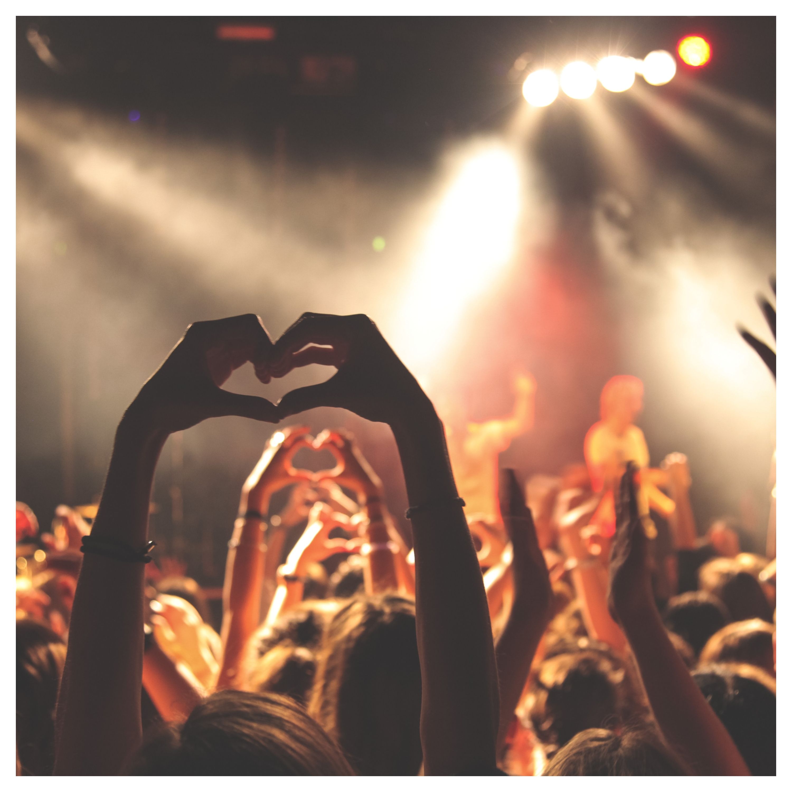 Une personne fait le signe coeur avec les doigts, au milieu d'une foule assistant à un concert
