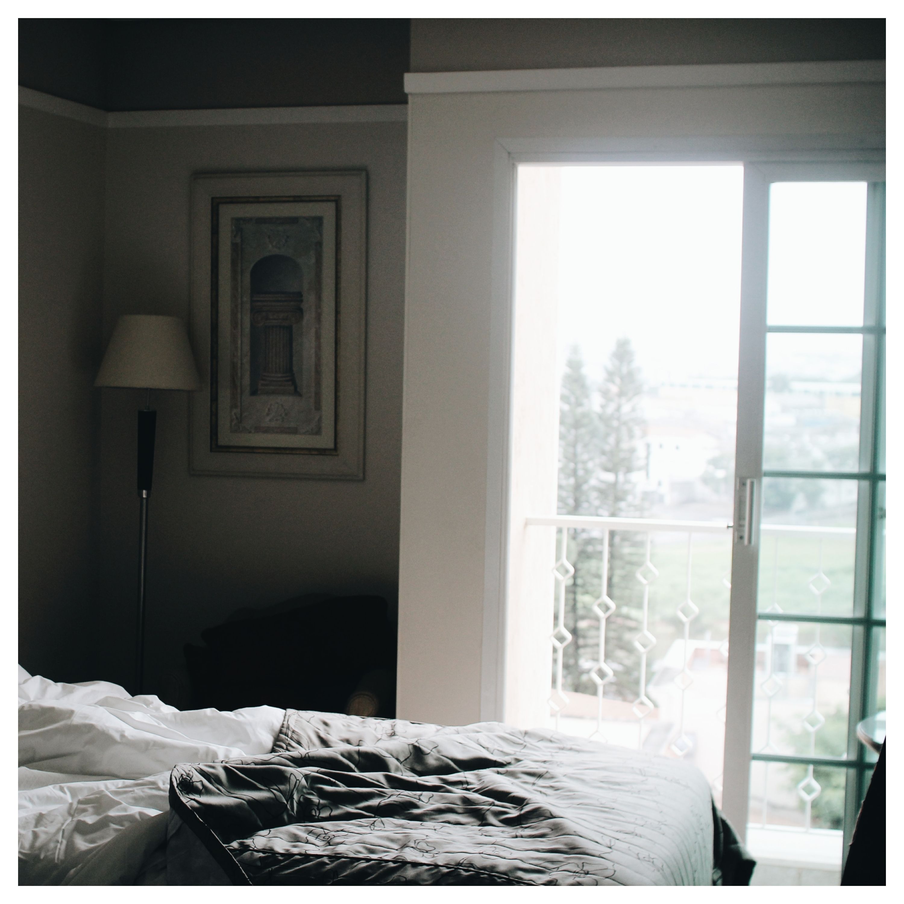Une fenêtre ouverte donne sur un balcon, vue depuis une chambre avec un lit défait