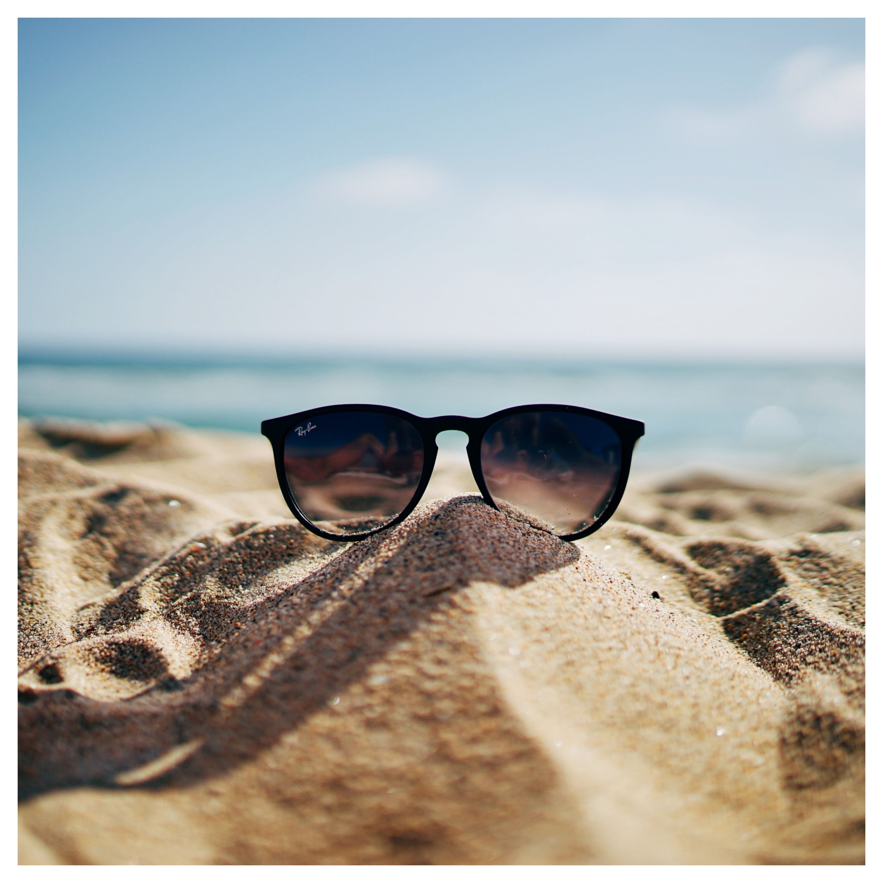 Paire de lunettes de soleil posée sur du sable, avec la mer en arrière-plan