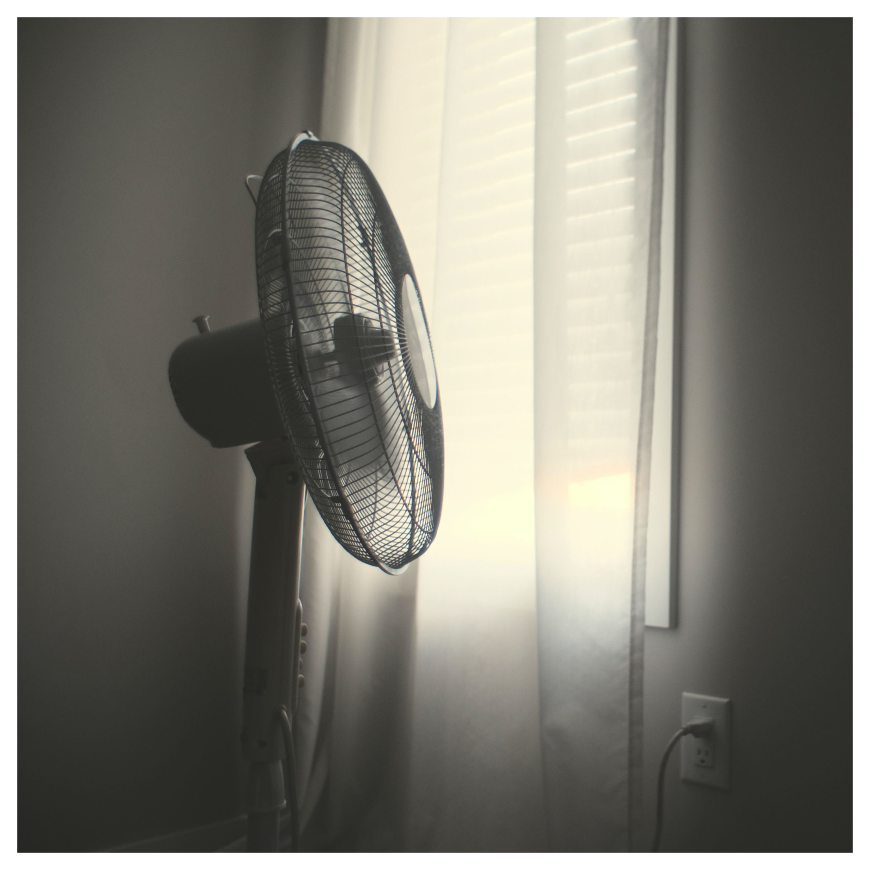 Un ventilateur branché dans une pièce avec un volet baissé