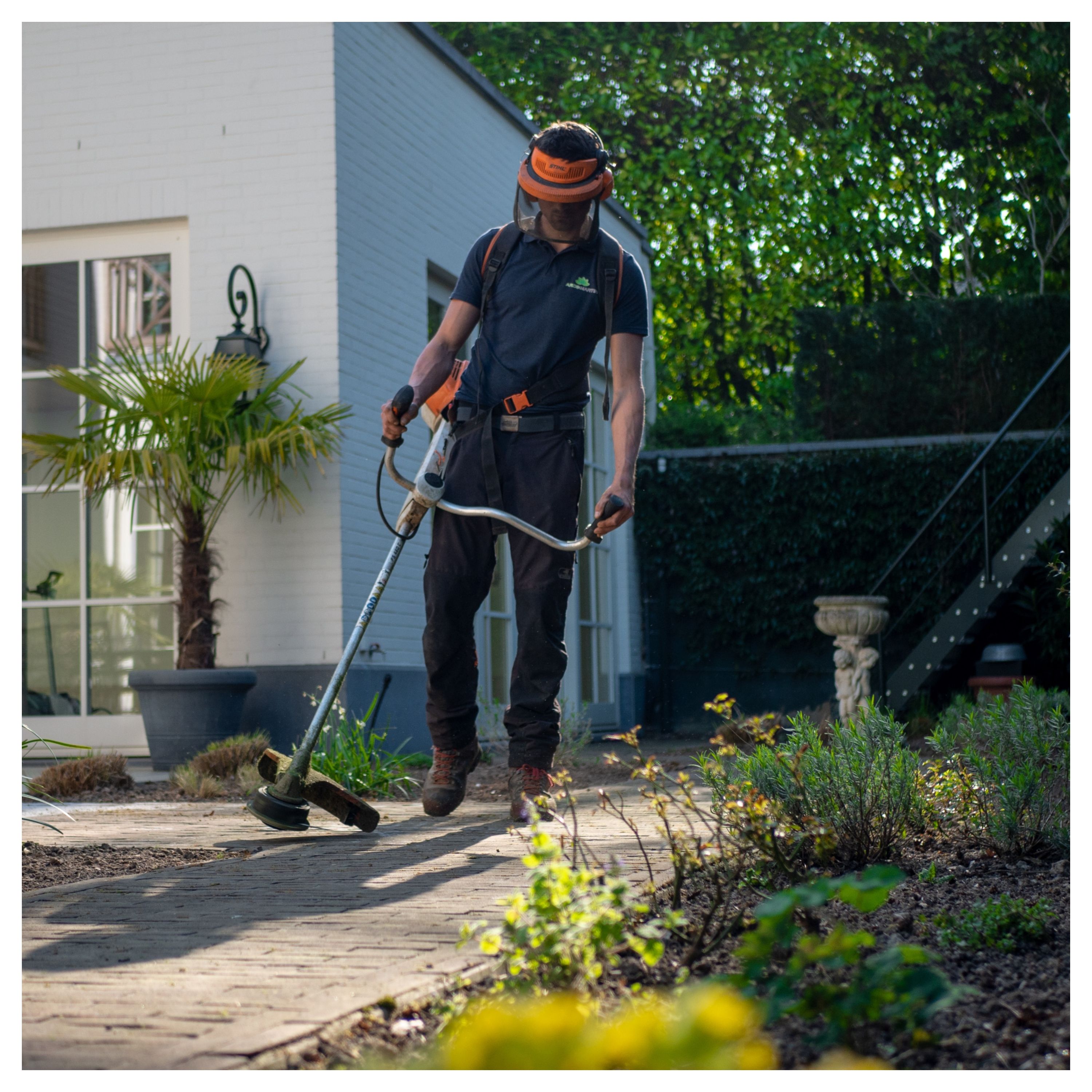 Un homme en train de désherber son jardin, avec un équipement de jardinier, lunettes, gants et protection