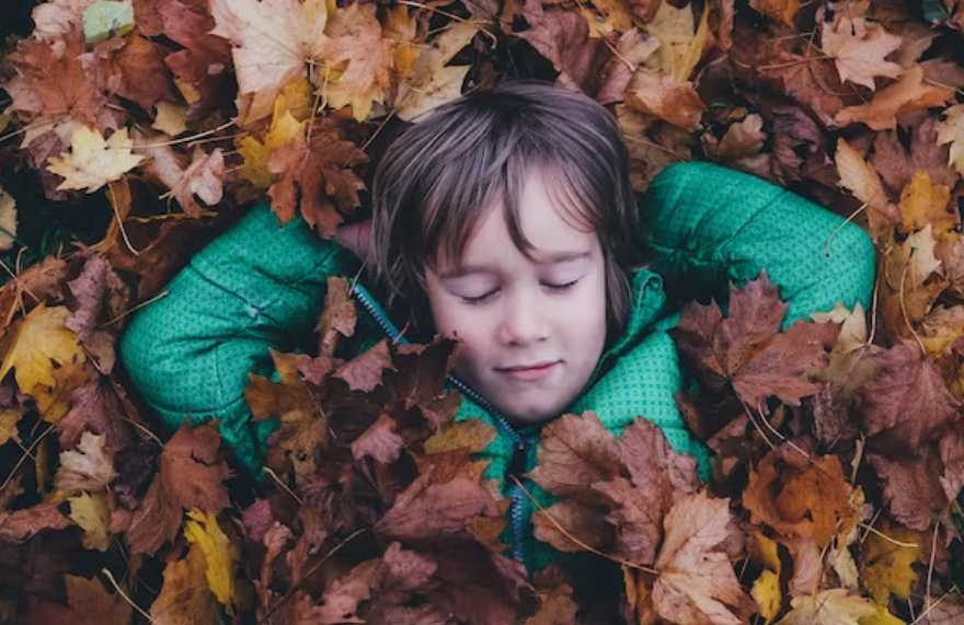 Un petit garçon ferme les yeux allongés dans des feuilles d'automne