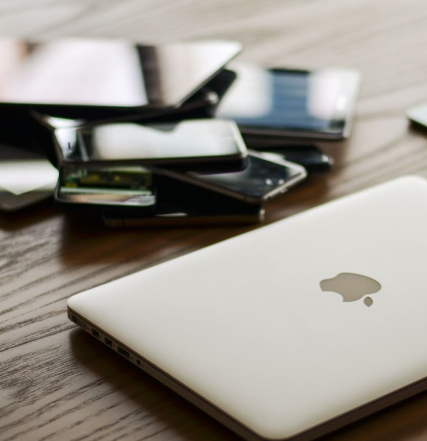 Bureau avec un MacBook en premier plan et une pile de smartphones et de tablettes