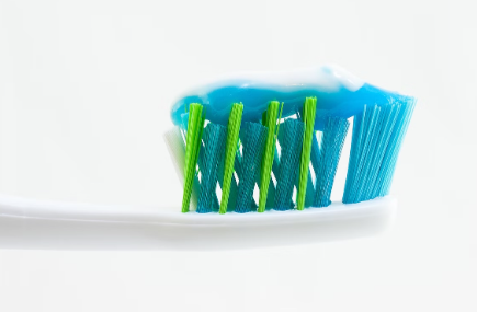 Pâte à dentifrice disposée sur une brosse à dents aux poils bleus et verts