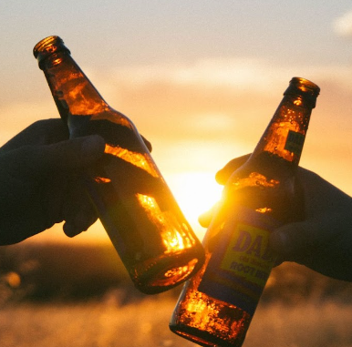 Deux bouteilles en verre trinquent l'une contre l'autre, coucher de soleil en fond