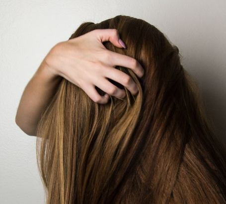 Une personne aux cheveux longs bruns passe sa main dans les cheveux
