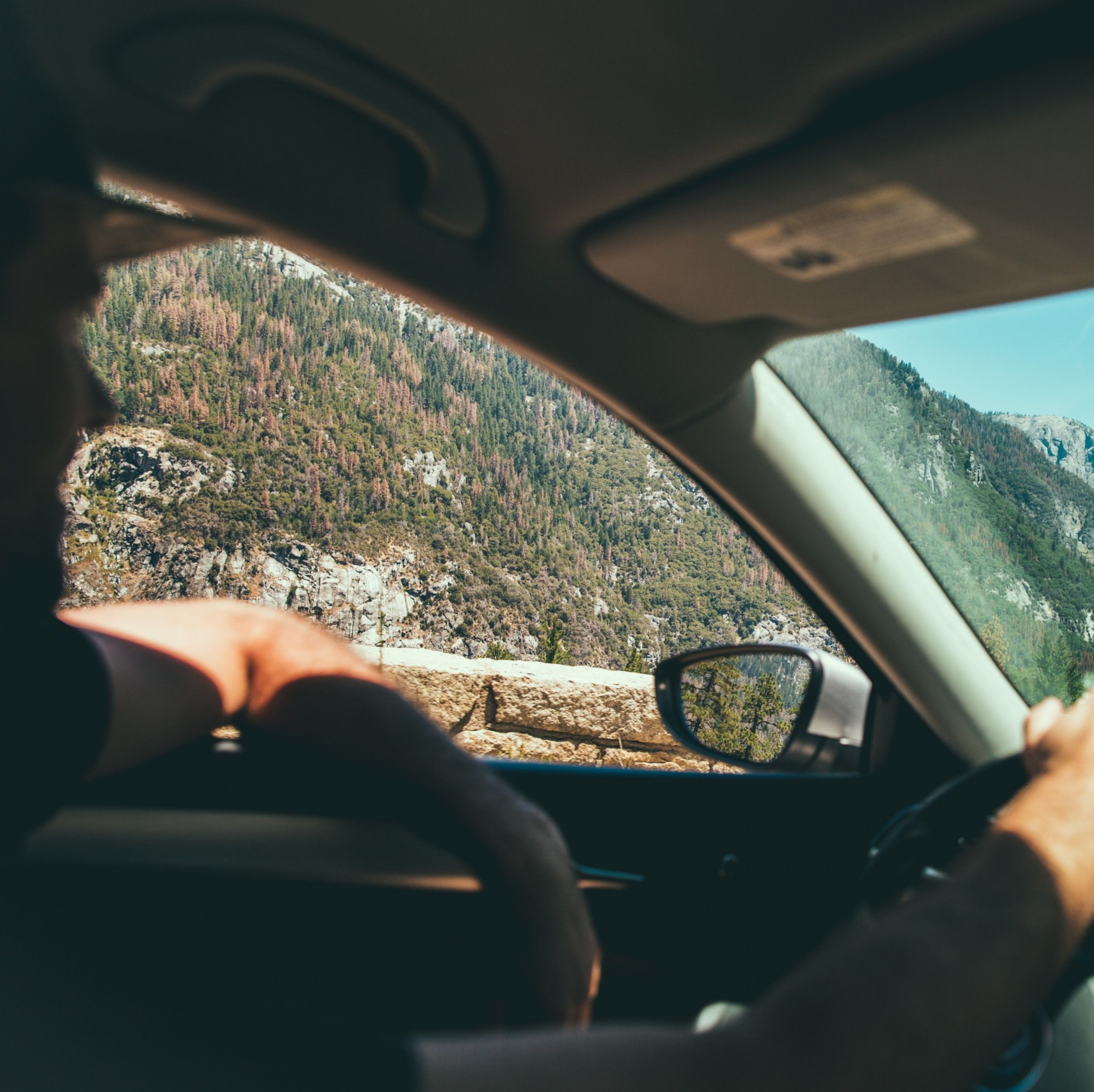 Un homme en train de conduire. Montagnes visibles depuis sa vitre.