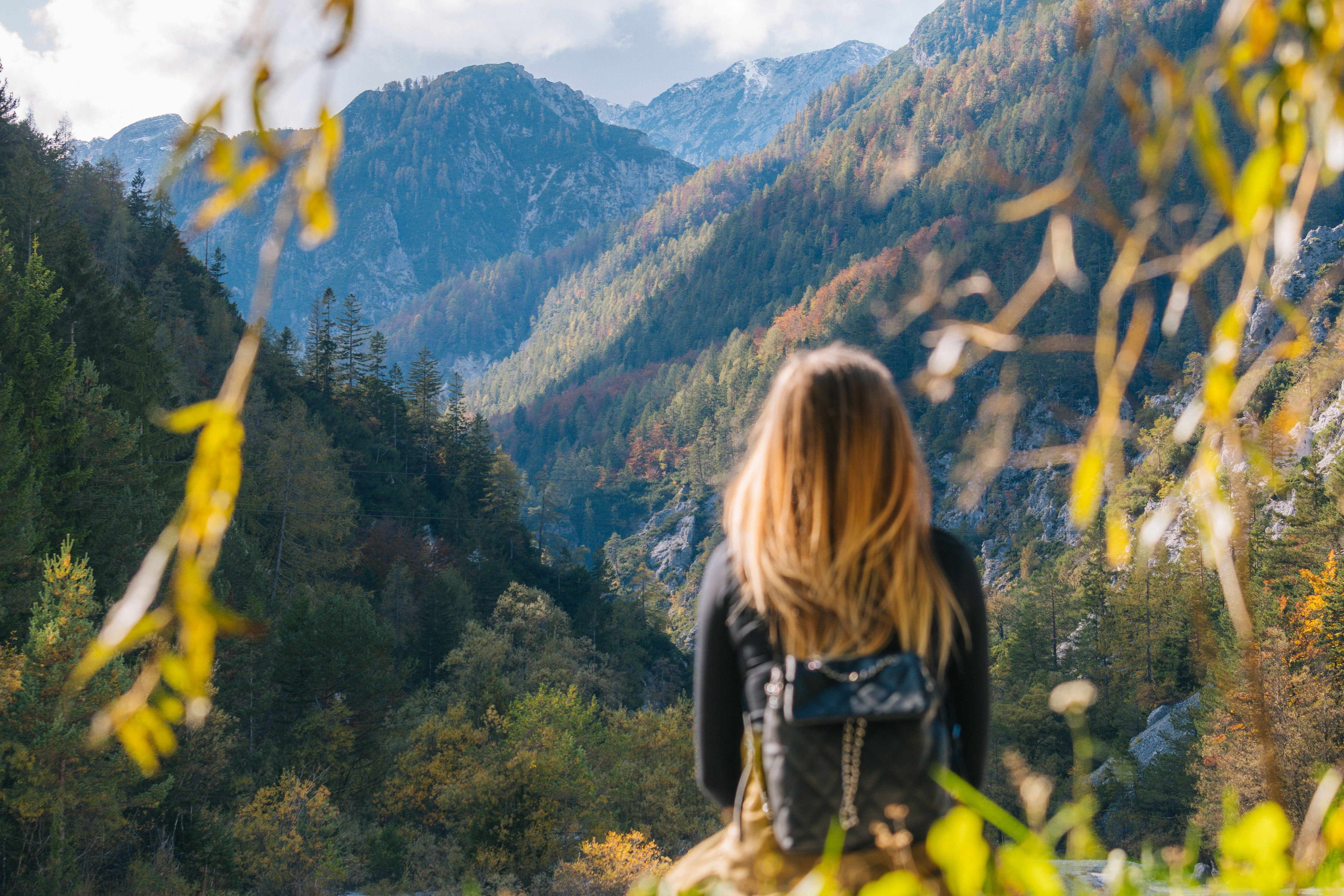 Une personne aux cheveux longs blonds assise observe des montagnes en arrière-plan