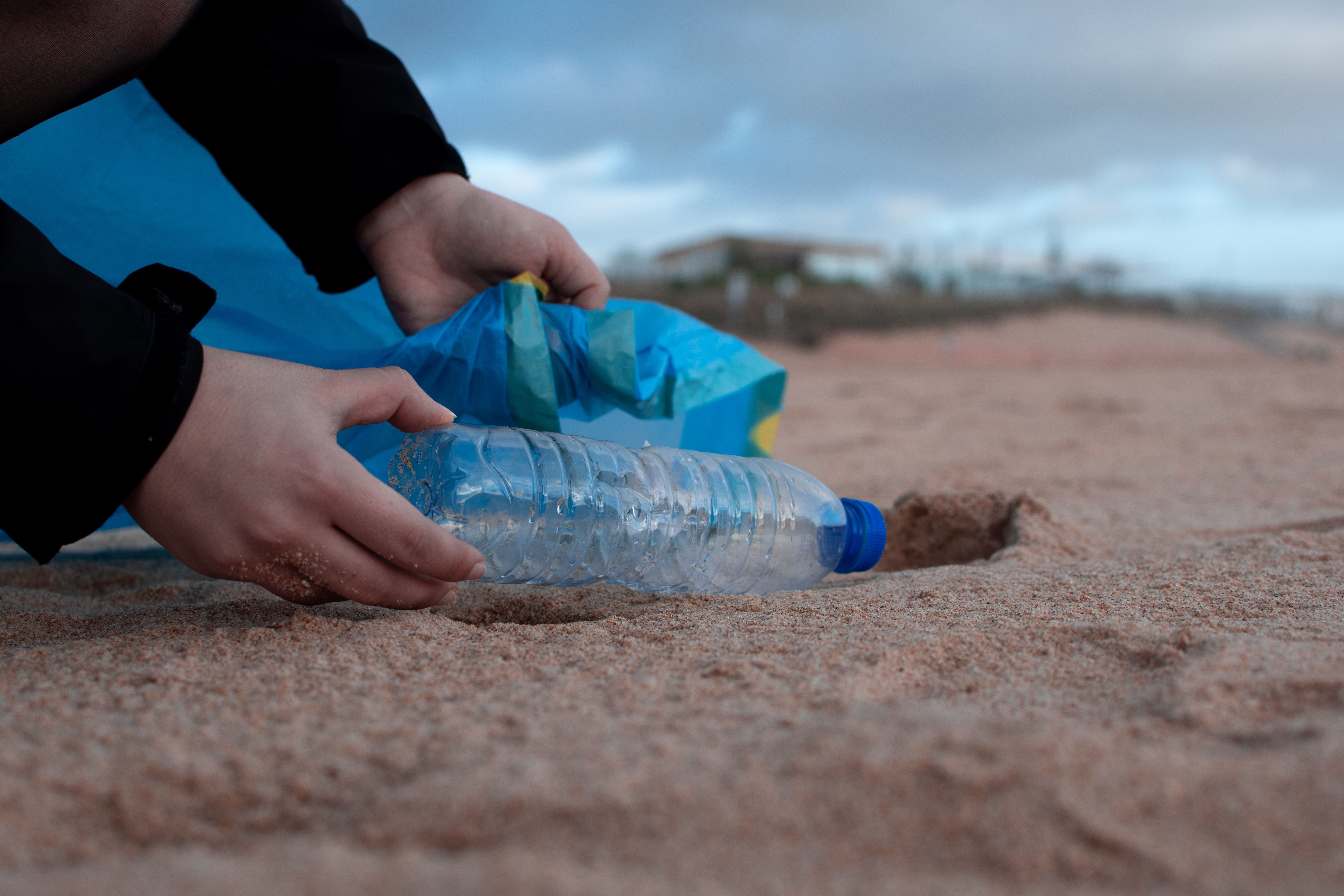 Une personne ramasse une bouteille d'eau en plastique sur une plage