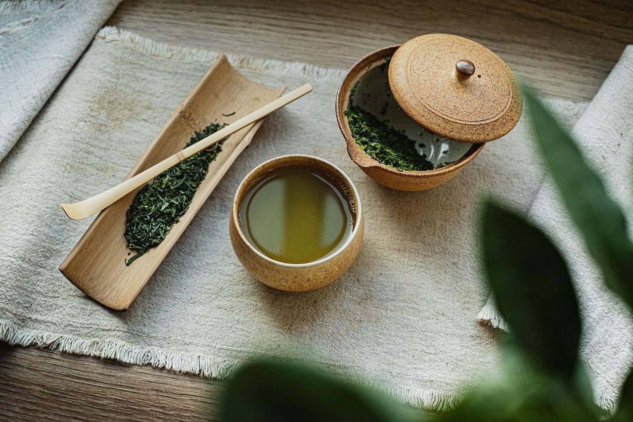 Sur un set de table en lin, on peut voit un bol avec du thé et un bocal avec de l'herbe verte.