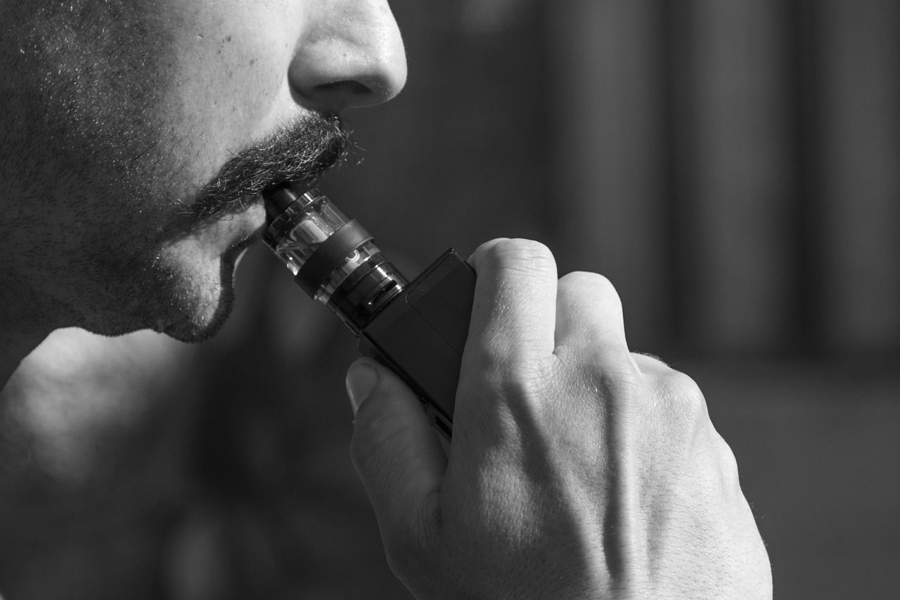 Un homme moustachu tire une vape sur sa cigarette électronique